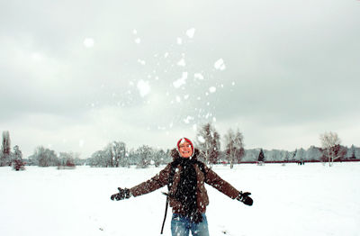 Smiling woman playing with snow while standing against sky