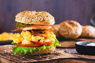 Homemade bagel with scramble egg, bacon, cheese, tomato and lettuce on a board