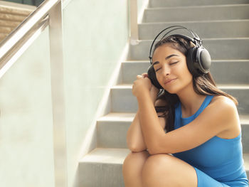 Portrait of young woman sitting on staircase listening to music