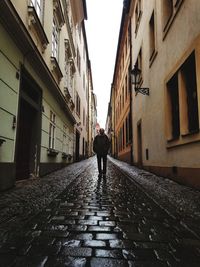 Rear view of man walking on footpath amidst buildings