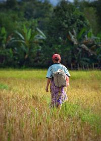 Rear view of woman with backpack walking on field