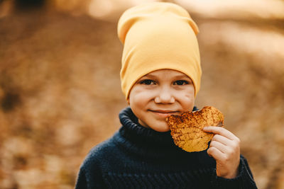 Portrait of a boy child in a warm hat walking holding an autumn leaf in the fall forest outdoors