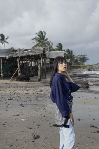 Young woman standing on beach against sky