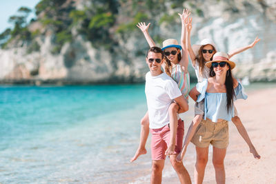 Parents piggybacking daughters at beach