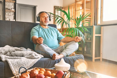 Mature middle-aged overweight man in wireless headphones relaxing at home with guided meditation.