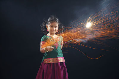 Girl spinning sparkler while standing against black background