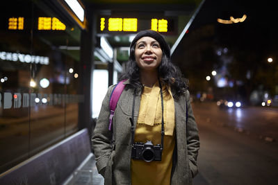 Portrait of smiling young woman standing on street at night