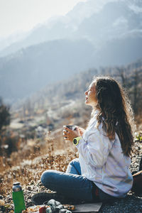 Woman with tea cup sitting cross-legged on mountain