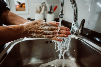 Cropped image of man washing hands in sink