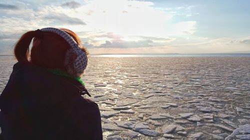 Close-up of woman wearing headphones at beach against sky during winter