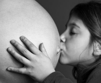Close-up of girl kissing pregnant mother abdomen