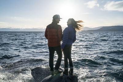 Young couple in love stand on rock in lake tahoe in the winter