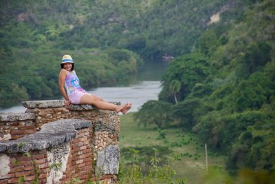 Portrait of happy woman sitting on ruined wall against forest