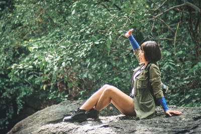 Full length of woman sitting on rock against plants