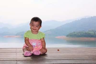 Portrait of cute boy sitting on lake against mountain