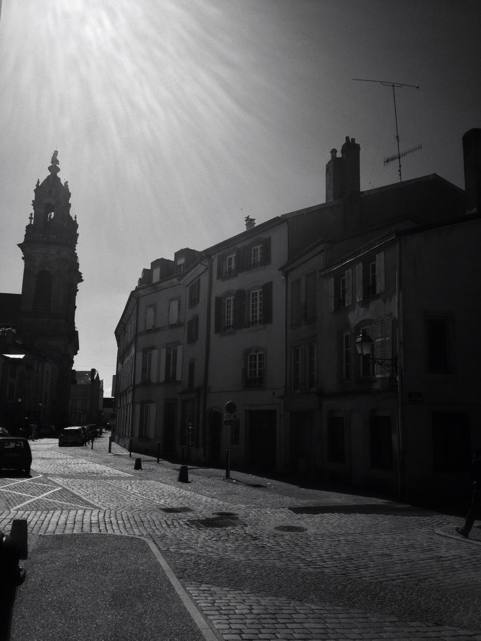 building exterior, architecture, built structure, street, road, cobblestone, city, the way forward, sky, transportation, street light, sunlight, incidental people, car, sidewalk, building, outdoors, residential building, city street, residential structure