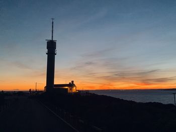 Silhouette tower by building against sky during sunset