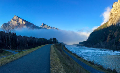 Panoramic view of road by mountains against blue sky
