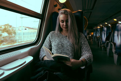 Full length of young woman sitting in train