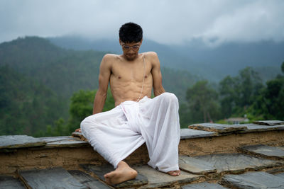 Full length of shirtless young man sitting outdoors