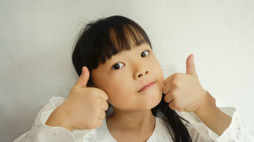 Close-up portrait of cute girl gesturing against wall