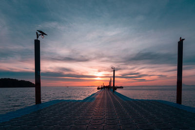 Street light by sea against sky during sunset