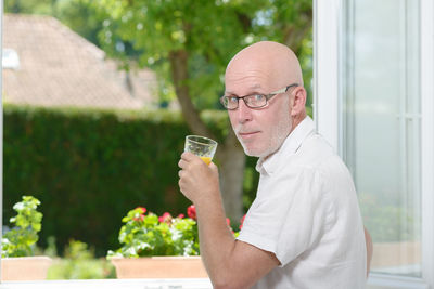 Portrait of man holding drink while standing at home