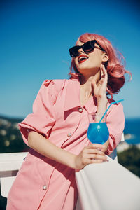 Young woman wearing sunglasses standing against sky