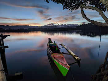 Boat moored in lake against sky during sunset