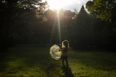 Girl playing with umbrella on grassy field in park