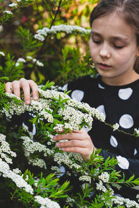 Cute girl holding flowering plant while standing outdoors