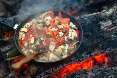 Frying chicken with vegetables in pan on fire. winter picnic in a forest