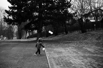 Rear view of boy in warm clothing with bucket walking on street