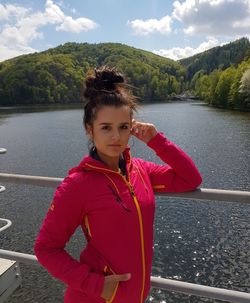 Portrait of young woman standing by lake against mountain