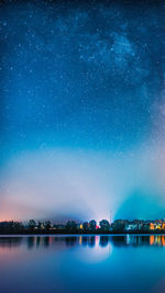 Illuminated buildings by lake against sky at night