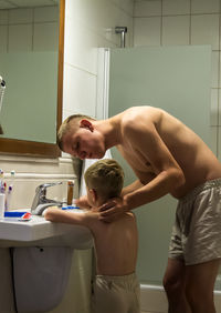 Father helping son while brushing teeth in bathroom