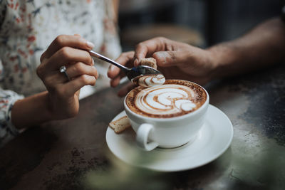 Cropped hand of man and woman by coffee at table