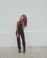 Woman wearing sunglasses standing on sidewalk against white wall