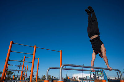 Shirtless man doing handstand on parallel bars at sports ground. 