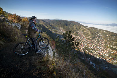 Cyclist looking at city while standing on cliff