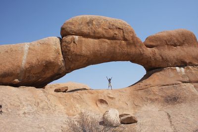 Low angle view of woman standing on rock formations against clear blue sky