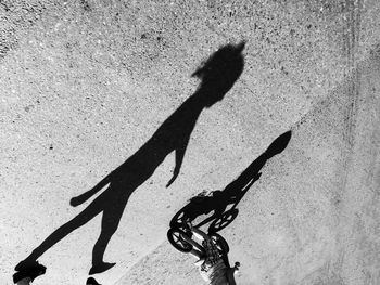 Shadow of girl walking while boy riding bicycle on footpath