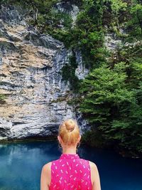 Rear view of woman standing on rock against trees