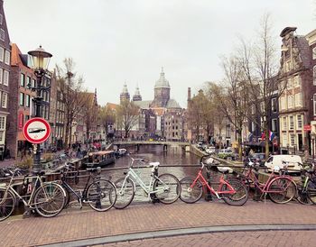 Bicycles parked on bridge over canal by buildings in city