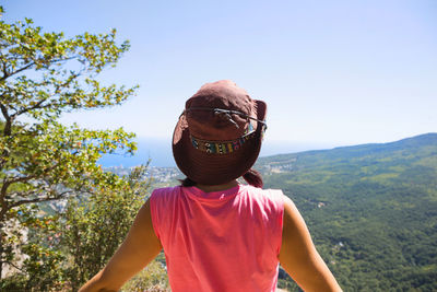 Woman in a hat looks at the panoramic view from the mountain to the sea and the 