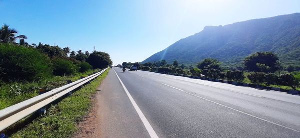 Empty road along trees and mountains against sky