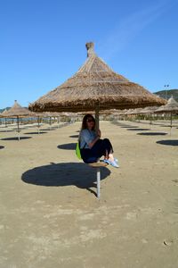 Woman sitting under thatched roof against blue sky