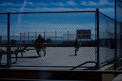 Sign on chainlink fence with people at playground against sky