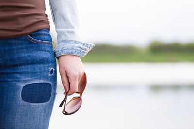 Midsection of woman holding sunglasses standing outdoors