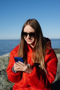 Young woman using mobile phone while sitting at beach